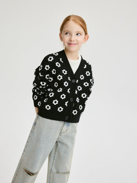 Person wearing a black cardigan with white floral pattern on a plain background