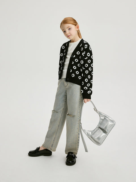 Young girl wearing a black floral cardigan, white shirt, and light blue jeans, holding a clear plastic bag on a white background.