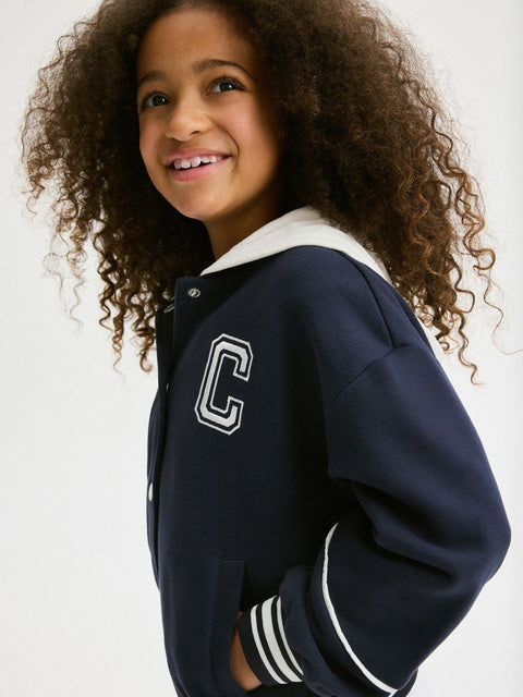 Child wearing a navy varsity jacket with a white 'C' emblem on a plain background