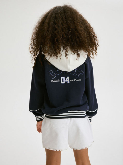 Person wearing a navy blue hoodie with white text on the back, standing against a plain background