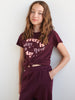 Person wearing a maroon t-shirt with text and matching pants against a white background