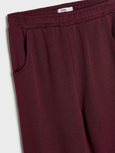 Maroon sweatpants with a brand label on a light gray background