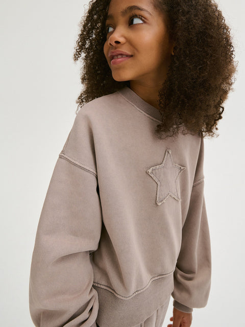 Person wearing a beige sweatshirt with a star design on a white background