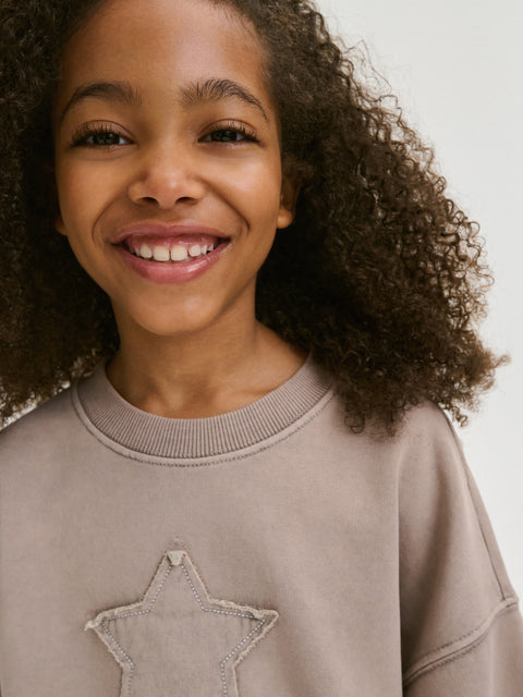 Child wearing a beige sweatshirt with a star design on a plain background