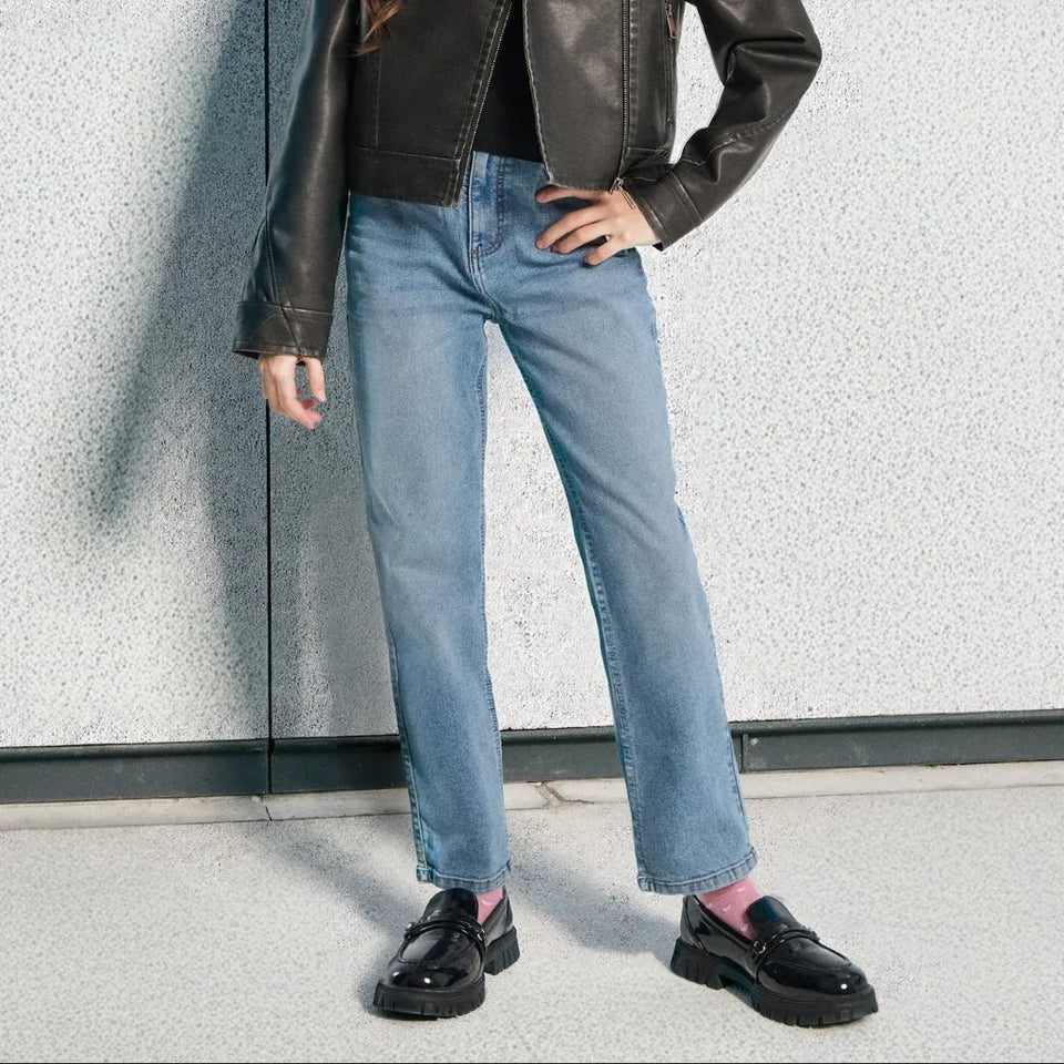 A person wearing light-wash blue straight-leg jeans, a black leather jacket, black loafers, and pink socks, standing against a textured light gray wall.