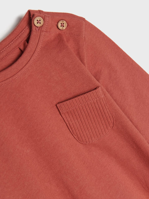 Close-up of a terracotta-colored shirt with a pocket and buttons on a light gray background