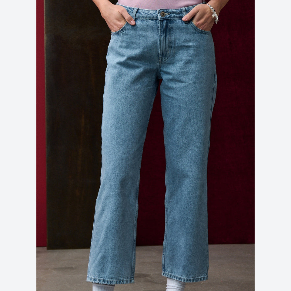 A person wearing light blue denim jeans with a straight-to-wide leg fit, standing against a dark red and brown background.