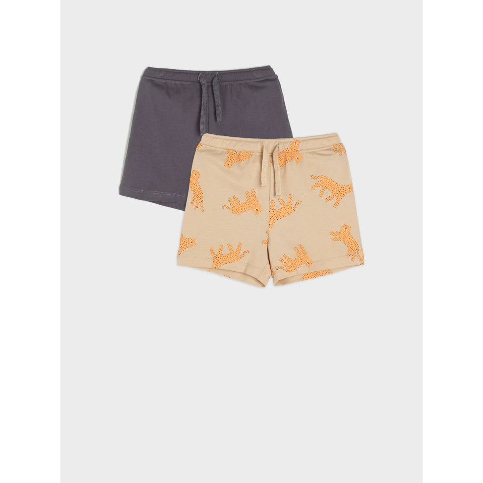 Two pairs of kids' shorts displayed flat against a light gray background. The front pair is beige with an all-over orange animal print, and the back pair is a solid dark gray.