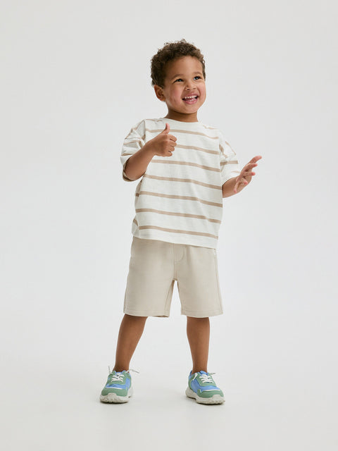 Child wearing a striped shirt and shorts, giving a thumbs-up on a white background