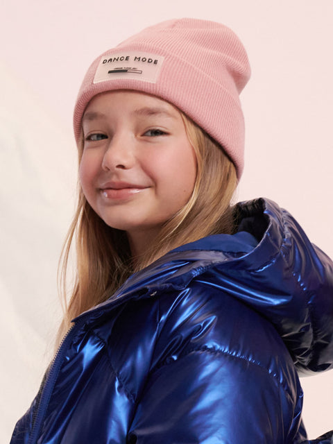 Young girl wearing a pink beanie with 'Dance Mode' text and a blue shiny jacket on a light background
