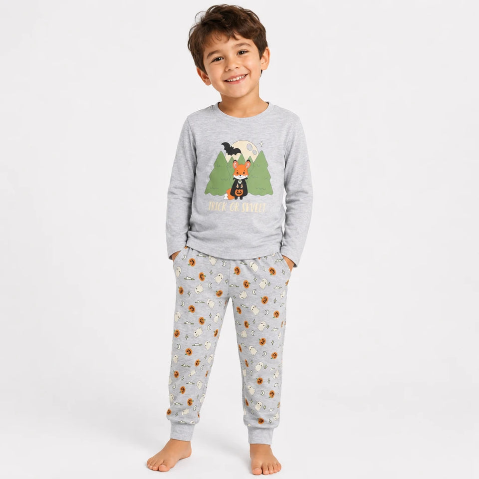 A young boy stands barefoot against a light gray studio background wearing a light gray long-sleeve pajama top with a forest and fox graphic, paired with matching gray pajama pants covered in a small brown and white animal print.