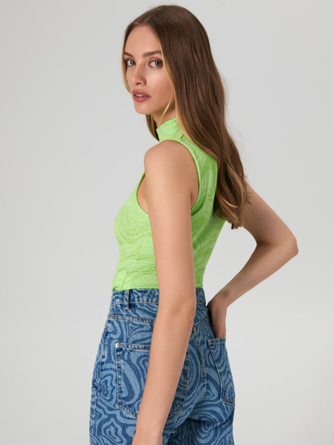 Woman wearing a green sleeveless top and blue patterned pants on a plain background