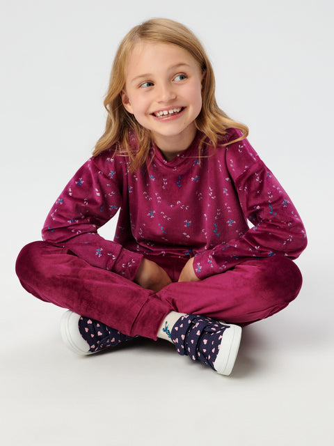 Young girl wearing a maroon tracksuit with floral patterns on a white background
