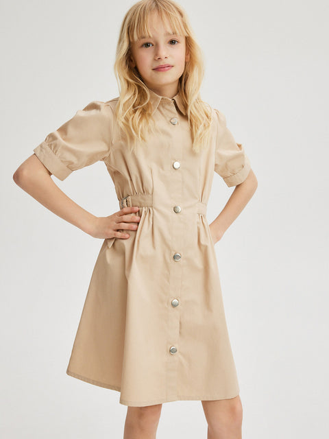 Young girl wearing a beige dress with buttons on a white background