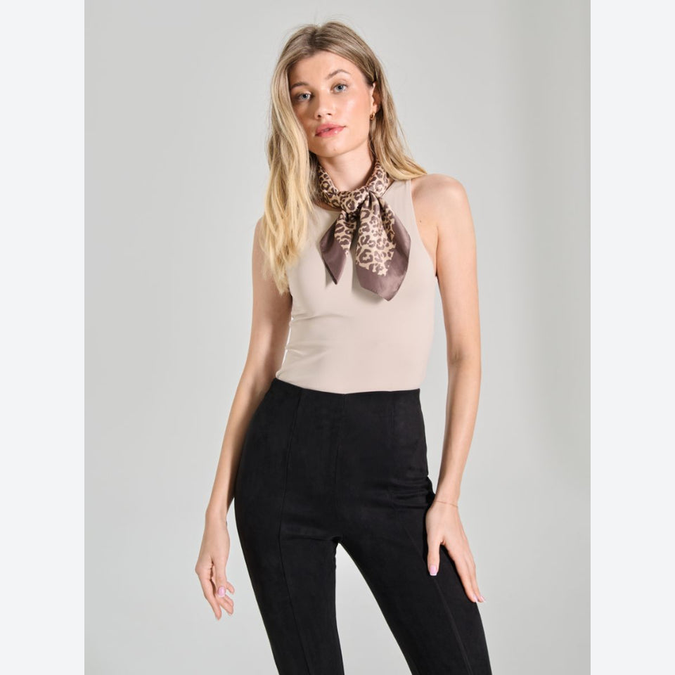 A woman modeling a beige sleeveless top and black pants, wearing a brown and beige leopard-print neck scarf, against a light gray studio background.