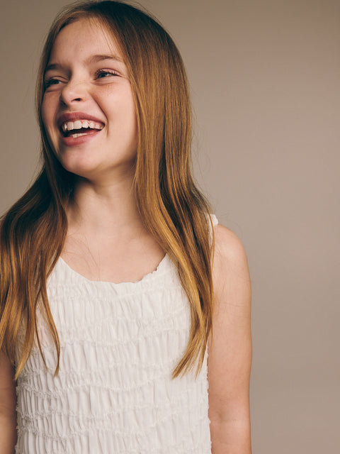 Young girl with long blonde hair wearing a white dress against a beige background