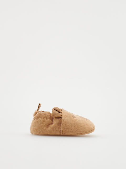 Tan baby shoe with a bow on a white background