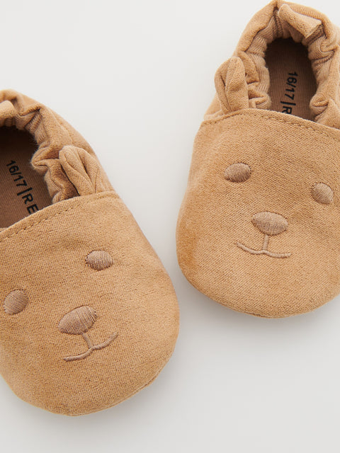 Pair of tan baby shoes with bear face design on a white background