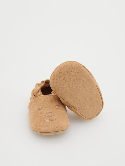 Pair of tan baby shoes with a bear face design on a white background