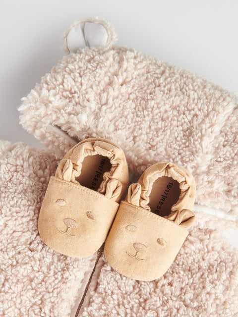 Pair of beige baby shoes on a soft pink surface