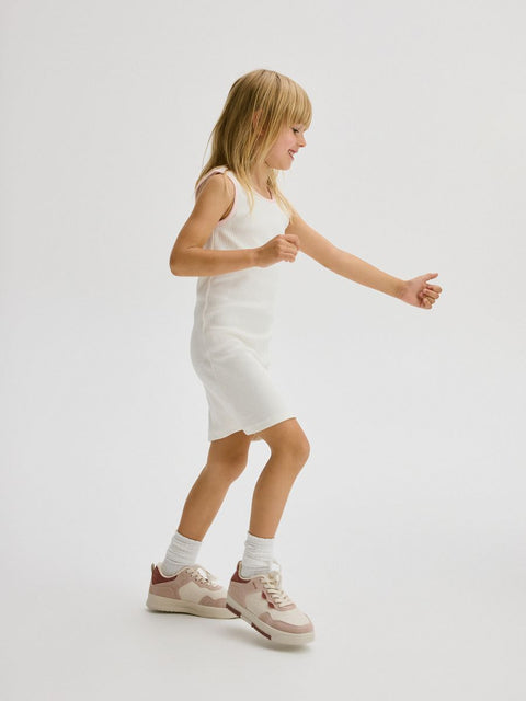 Young girl in a white dress standing on a plain background