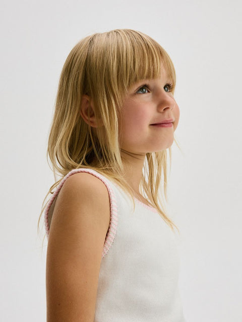 Young girl with blonde hair and a white top with pink straps on a light background