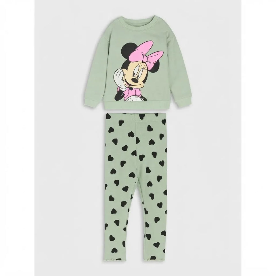 A two-piece children's pajama set featuring a light sage green sweatshirt with a Minnie Mouse graphic on the front, and matching sage green leggings with a black heart pattern, displayed on a light gray background.
