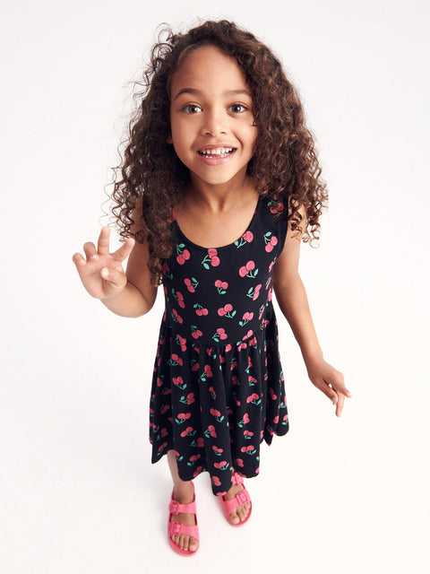 Young girl wearing a black dress with cherry pattern on a white background