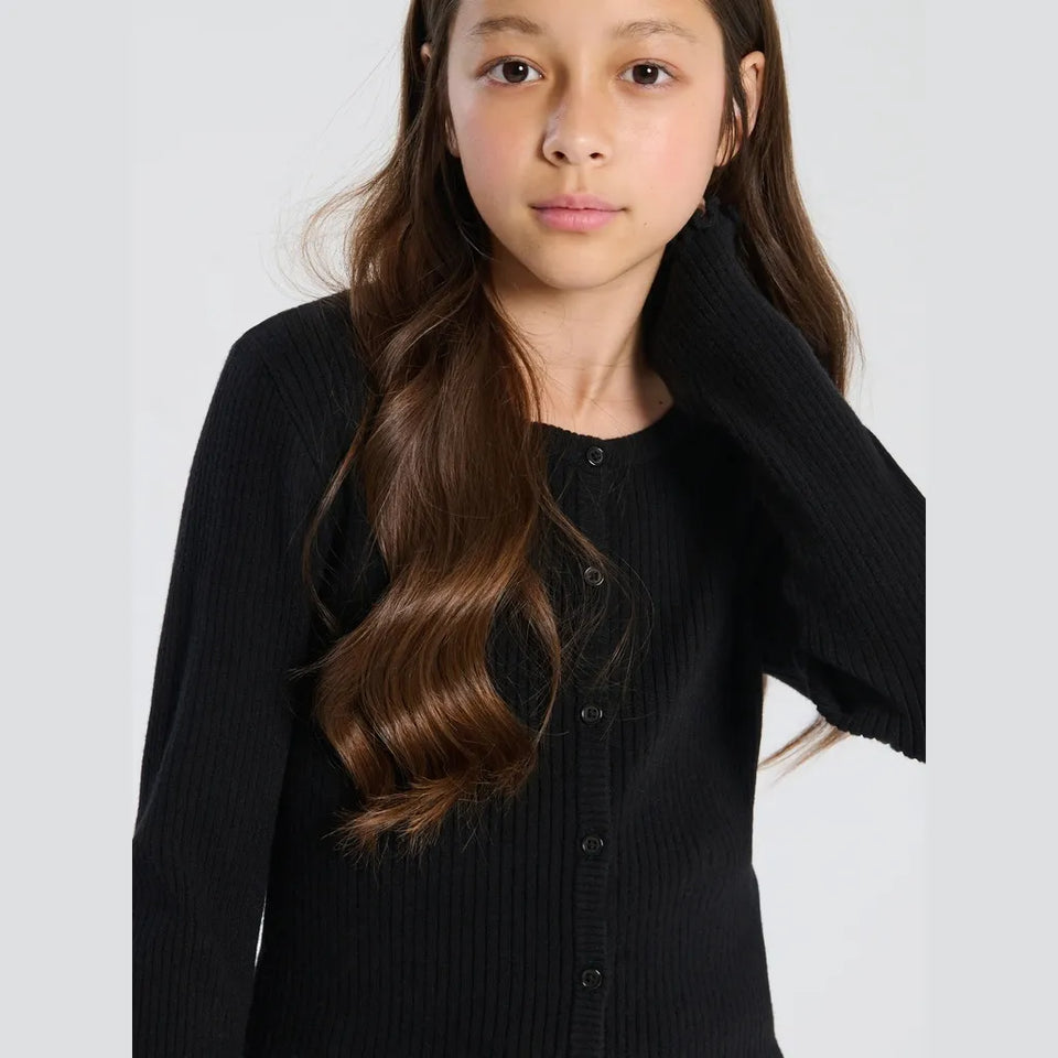 A young girl with long brown hair wearing a black ribbed button-up cardigan sweater, photographed against a light gray studio background.
