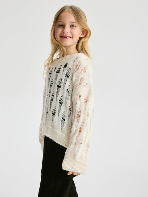 Young girl wearing a cream sweater with black text pattern on a white background