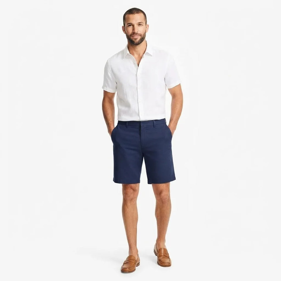 A man modeling a white short-sleeve button-down shirt and navy blue shorts against a clean white background.