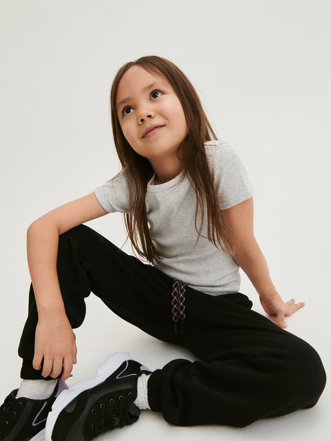 Young girl sitting on the floor wearing a gray t-shirt and black pants against a white background