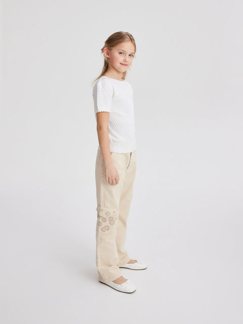 Young girl wearing a white top and beige pants on a light gray background