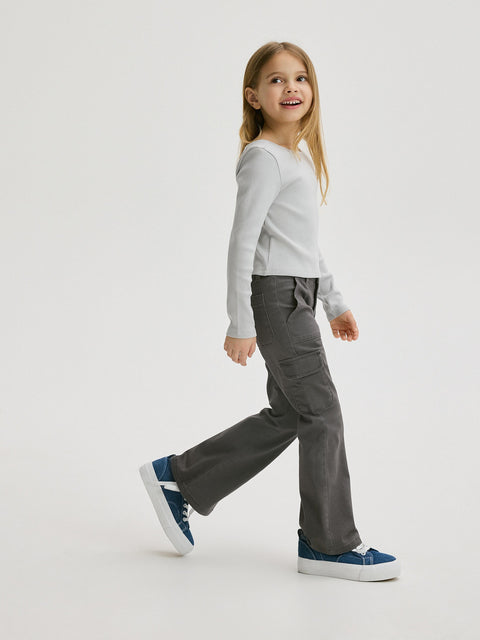 Young girl wearing a white long-sleeve shirt and gray pants on a white background
