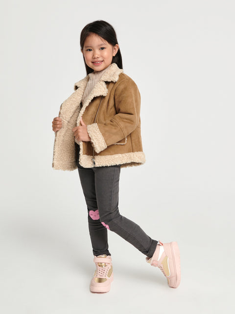 Young girl wearing a brown jacket with beige fur lining on a white background