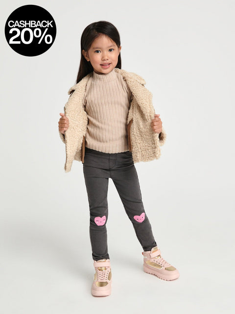 Young girl wearing a beige sweater, gray pants with pink hearts, and pink shoes on a white background with a cashback 20% offer.