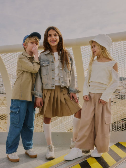 Three children standing together on a rooftop with a cityscape background