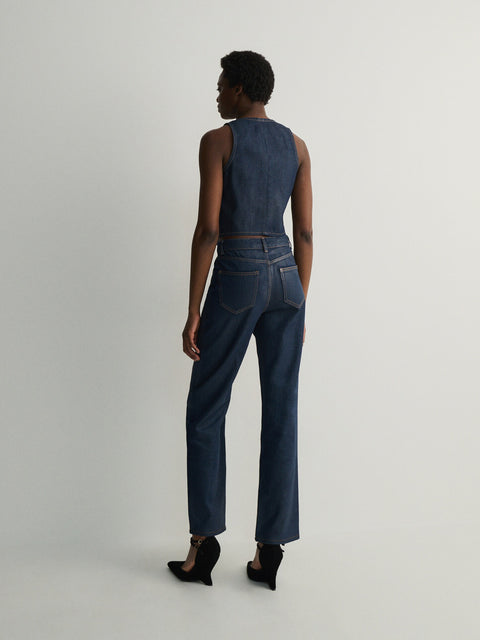 Person wearing a sleeveless denim top and high-waisted jeans on a plain background