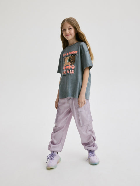 Young girl wearing a graphic t-shirt and light purple pants on a white background