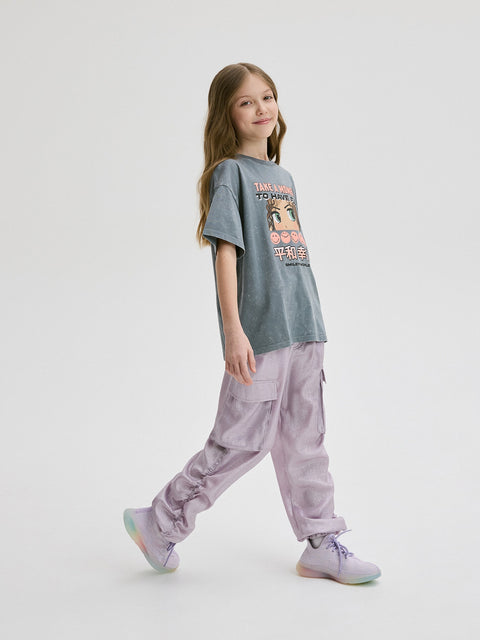 Young girl wearing a gray t-shirt with a graphic design and light purple cargo pants on a white background
