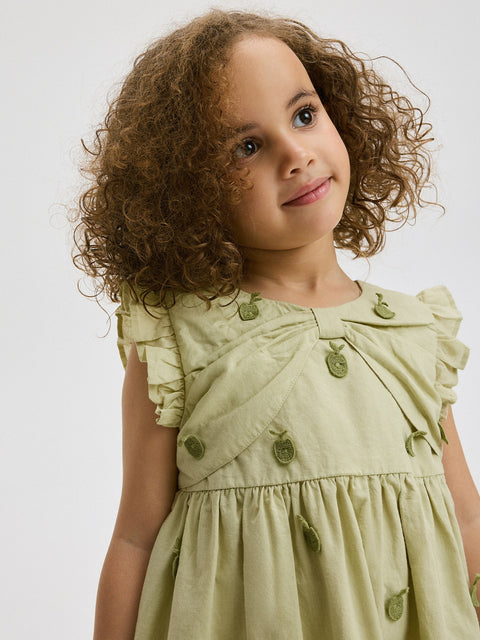 Child wearing a light green dress with buttons on a plain background