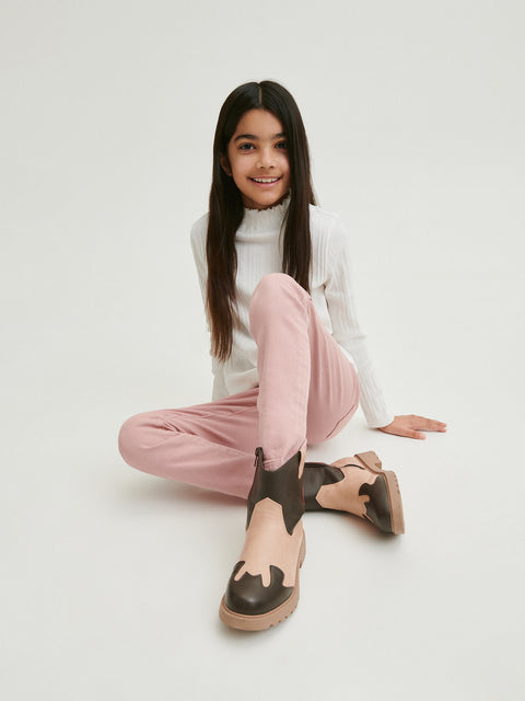 Person wearing a white turtleneck, pink pants, and brown shoes on a light gray background