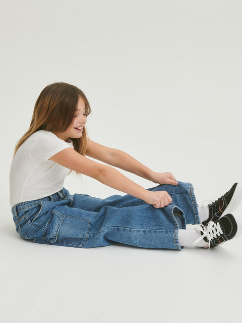 Person sitting on the floor wearing a white shirt, blue jeans, and black sneakers.