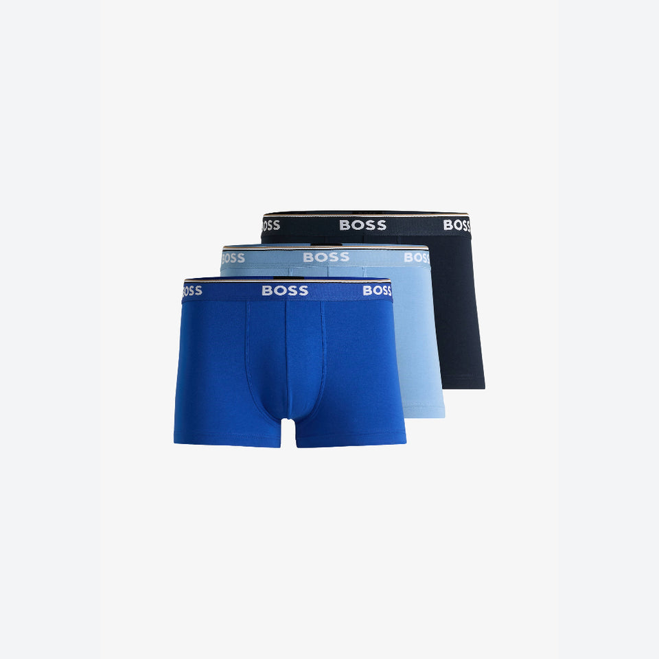 Three pairs of BOSS men's boxer briefs stacked together on a light gray background, showing the waistband branding. The front pair is a vibrant royal blue, the middle pair is a light blue, and the back pair is black.