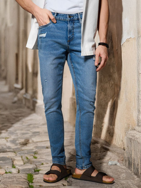 Person wearing blue jeans and sandals standing on a stone path.