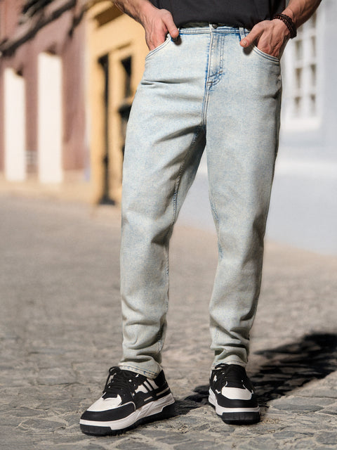 Person wearing light blue jeans and black sneakers on a street.