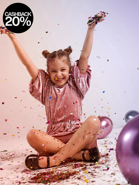 Child celebrating with confetti and balloons on a light pink background