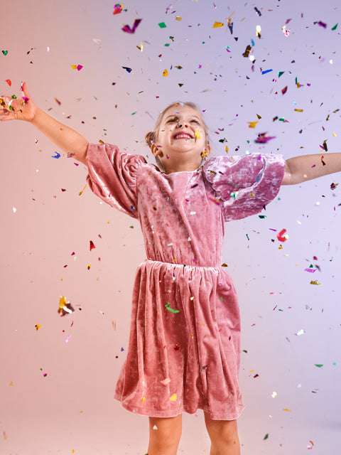 Child in a pink dress with confetti falling around them on a light pink background