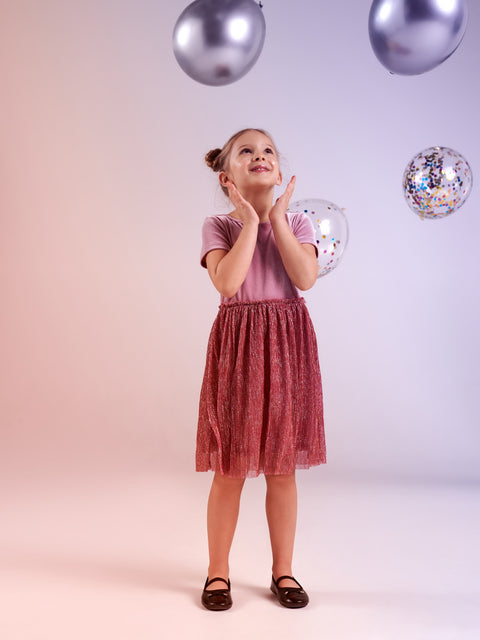 Young girl in a pink top and red skirt standing in front of balloons on a light background