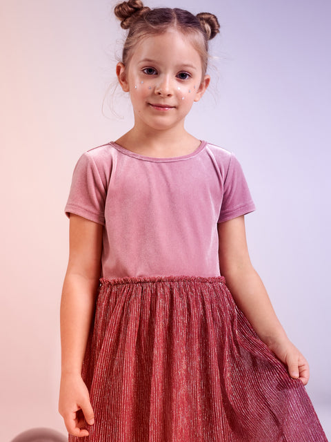 Young girl wearing a pink top and red skirt against a light background
